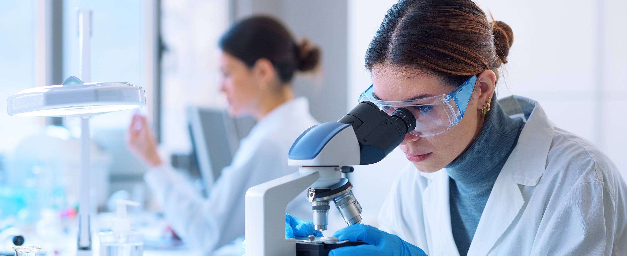 Researchers working in the clinical laboratory Young scientists conducting research investigations in a medical laboratory, a researcher in the foreground is using a microscope